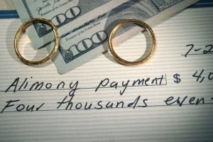 two wedding bands on top off two hundred dollar bills and a check that says alimony payment symbolizing Ft. Lauderdale alimony and spousal support payments 